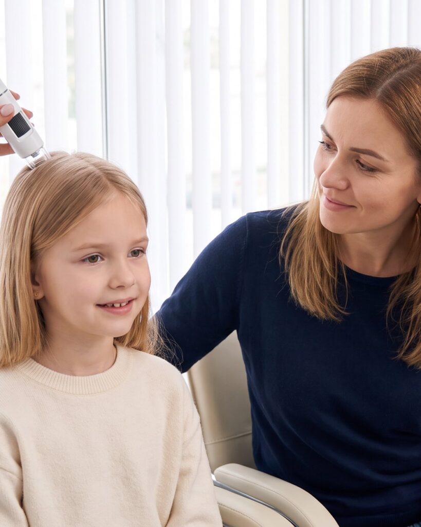 A young girl smiling during her scalp examination while her mother watches
