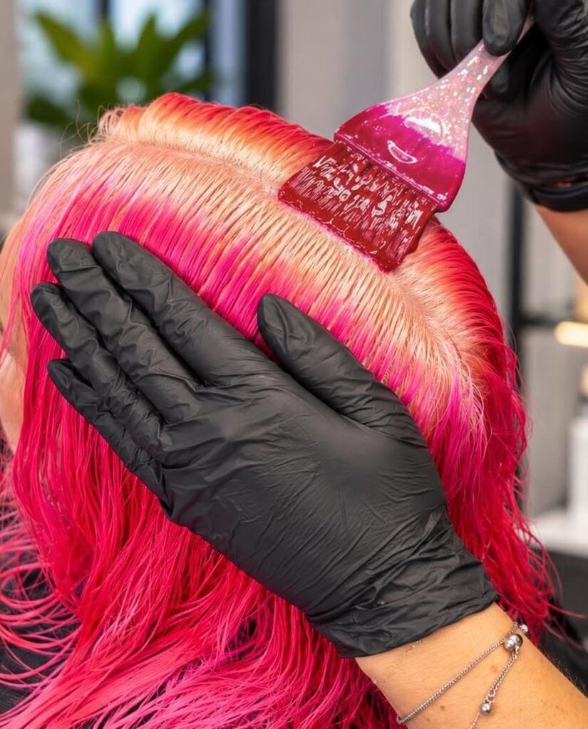 Gloved stylist brushing vivid pink colour onto a client’s roots