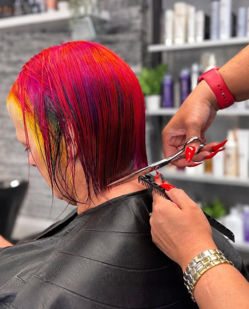 Stylist cutting a sleek bob in vivid red, pink and yellow colour at Chameleons