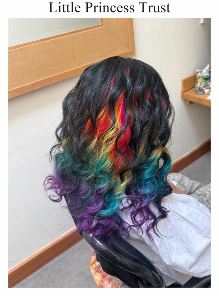 Little Princess Trust wig: black curls with rainbow-coloured sections, worn by a child