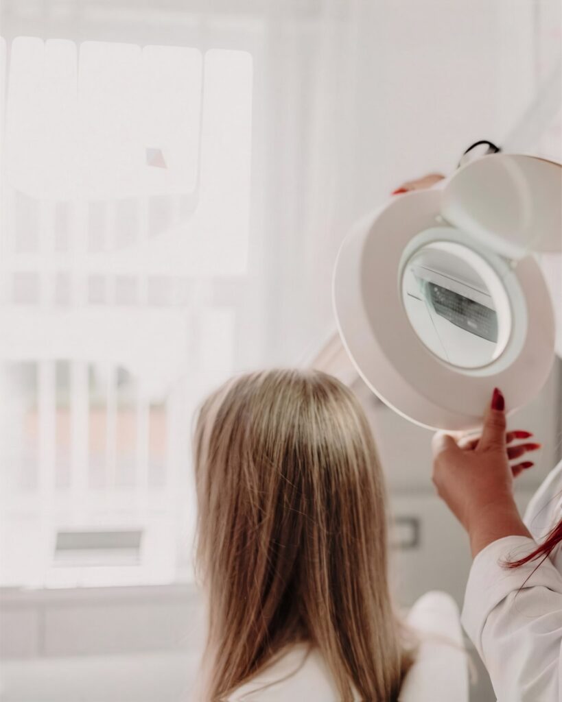 A trichologist examining a client’s hair through an illuminated magnifying lamp